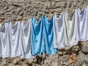 White and blue shirts hang on a laundry line that hangs along a rough stone wall.