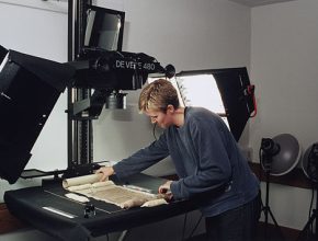 Color photograph of a person setting up a manuscript for digitization using an overhead camera and copy stand.