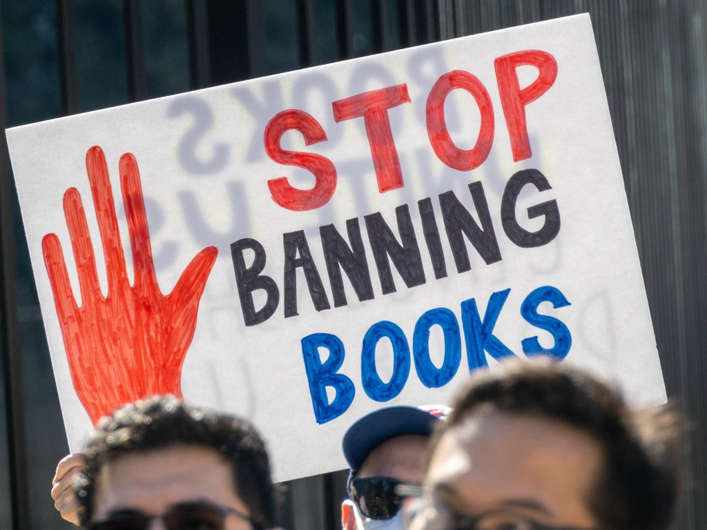 Hand lettered sign reads "Stop Banning Books". A red hand is also featured.