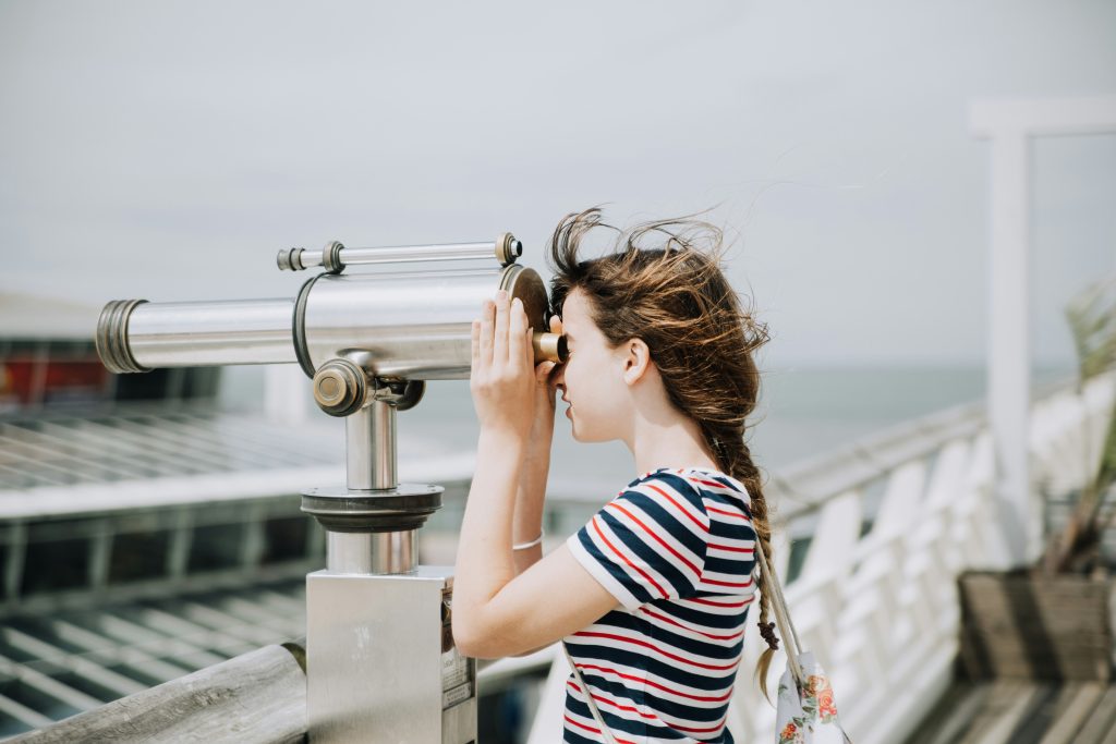 A young woman looks through a telescope to view a distant landscape