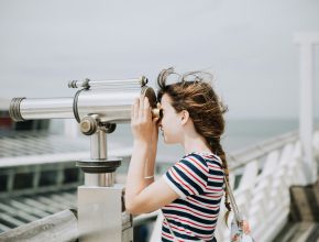 A young woman looks through a telescope to view a distant landscape